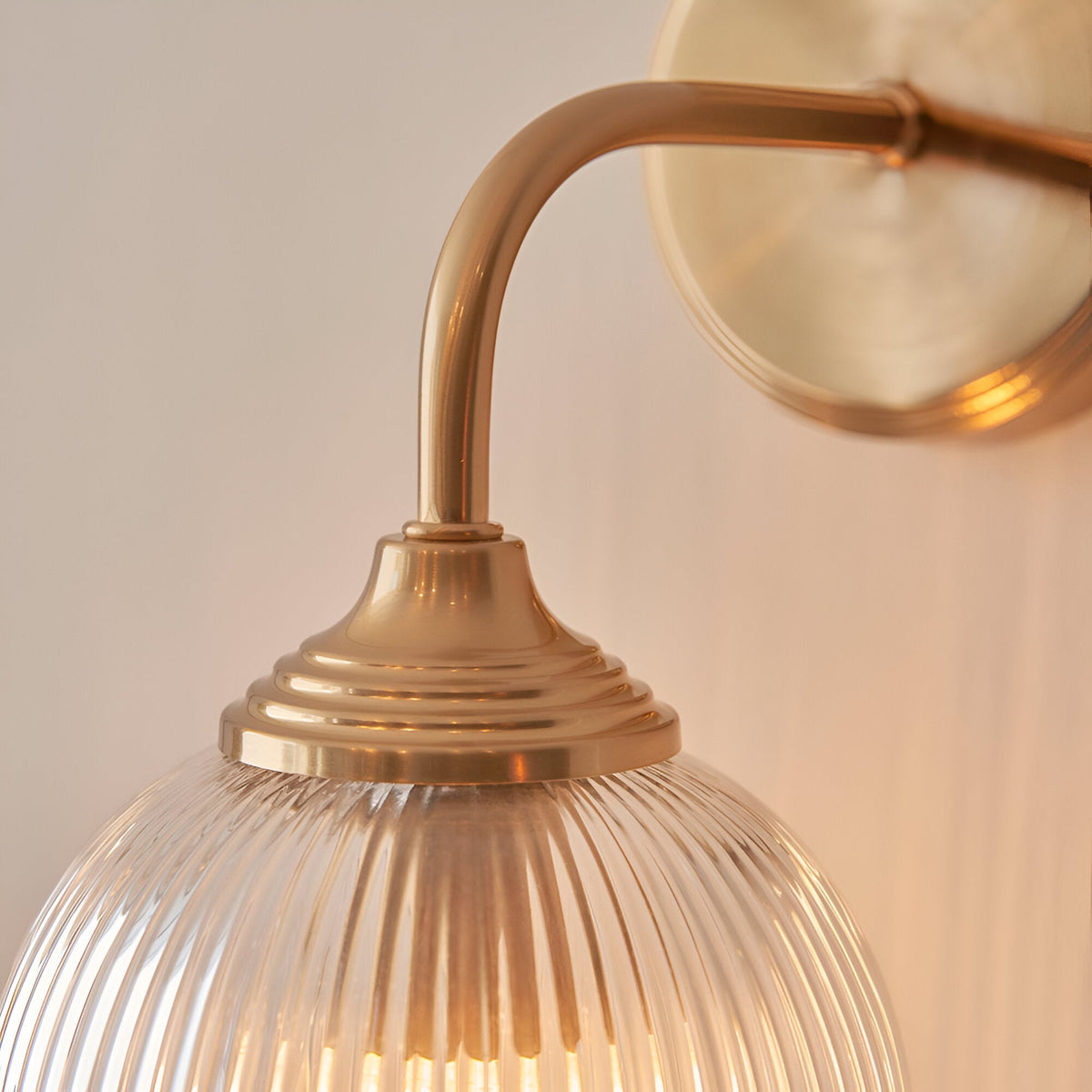 Endon Halstead brass wall light close-up showing the curved arm, round back plate and clear ribbed domed glass shade.