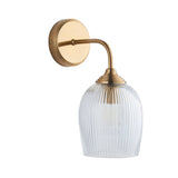 Endon Halstead single wall light in brushed brass with a curved arm, round back plate and clear ribbed domed glass shade, on a white background.