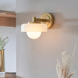 Endon Ashby brass wall light with frosted glass shade and opal sphere, mounted on a neutral wall in a styled interior setting.