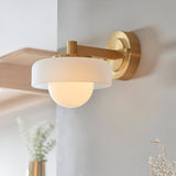 Endon Ashby wall light in brushed aged brass with a frosted glass drum shade encircling a matt opal glass sphere, mounted on a light interior wall.