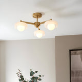 Endon Ashby 3 light semi-flush ceiling light in aged brass with three white glass shades on angled arms, installed in a warm neutral room.