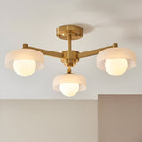 Endon Ashby 3 light semi-flush ceiling light in aged brass with three white glass shades and globe lamps on a triple-arm frame, mounted to a neutral ceiling.