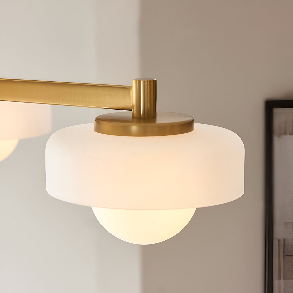 Close-up of Endon Ashby semi-flush ceiling light shade in aged brass with frosted glass tier and lit globe, mounted beside a framed picture.
