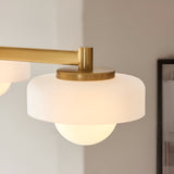 Close-up of Endon Ashby semi-flush ceiling light shade in aged brass with frosted glass tier and lit globe, mounted beside a framed picture.