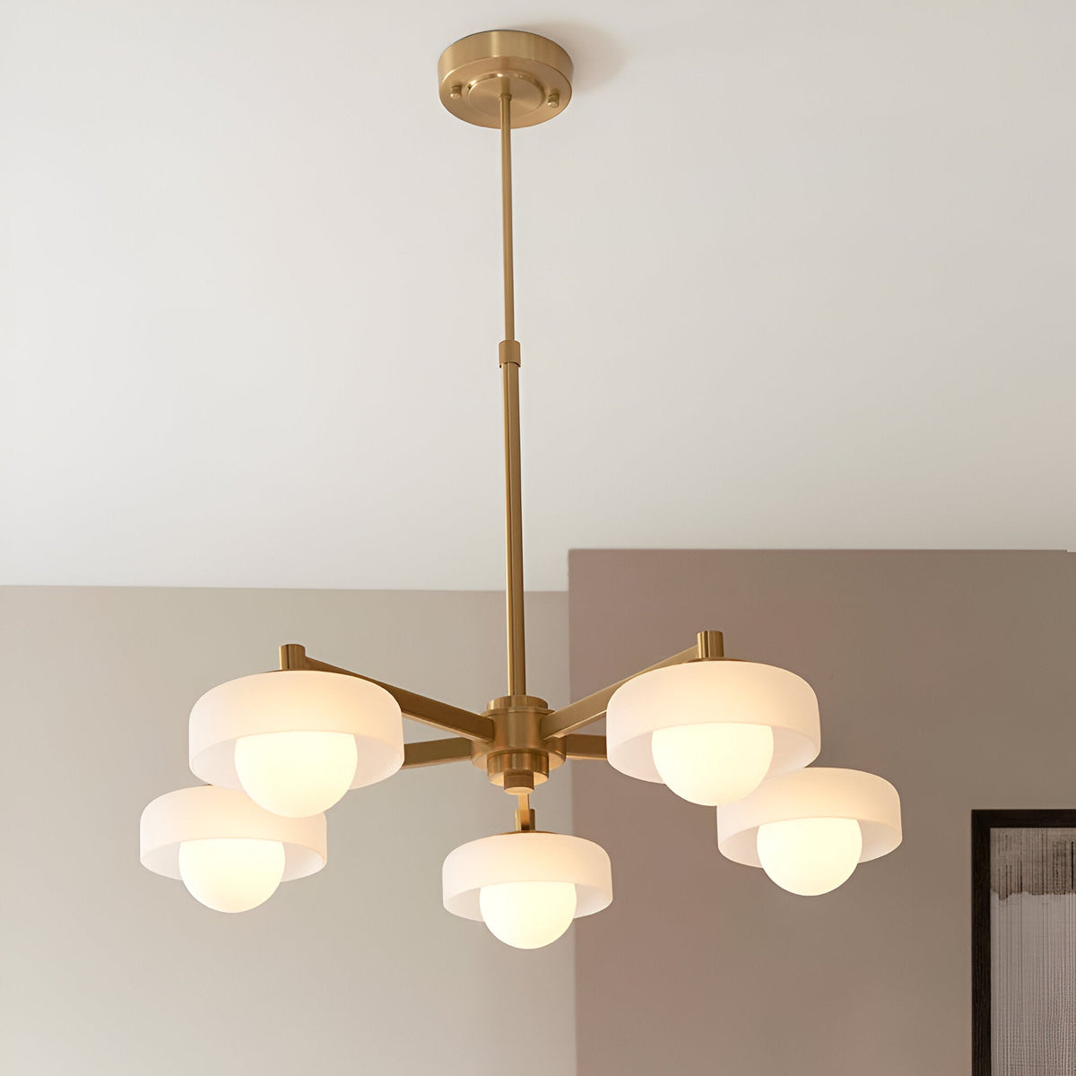 Endon Ashby 5 light pendant in brushed aged brass with frosted glass shades and opal inner globes on a telescopic stem, in a neutral room.