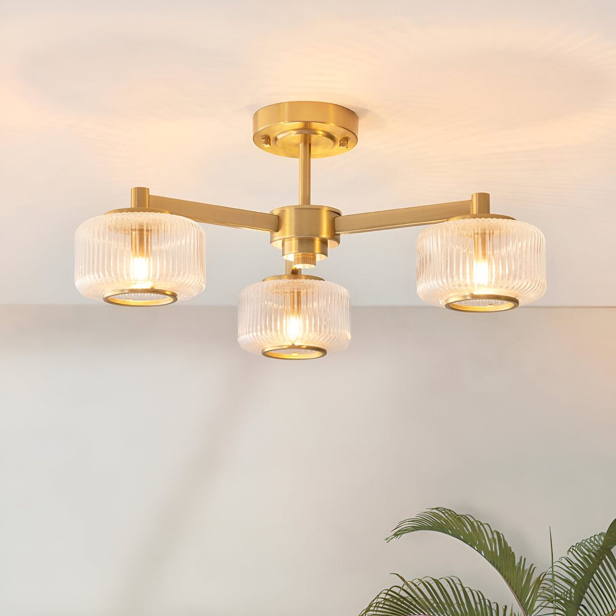 Endon Rutland 3 light semi-flush ceiling light in aged brass with ribbed glass shades on three arms, mounted to a pale ceiling.