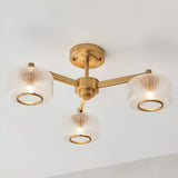 Endon Rutland 3 light semi-flush ceiling light in aged brass with ribbed glass shades on three arms, mounted to a white ceiling.