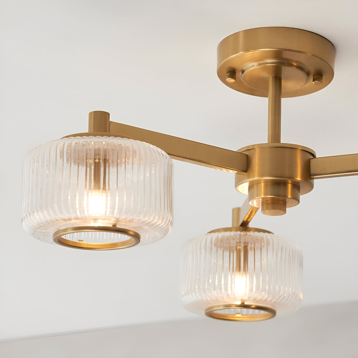 Endon Rutland semi-flush ceiling light in aged brass, shown close-up with ribbed glass shades on angled arms fixed to a round ceiling plate.