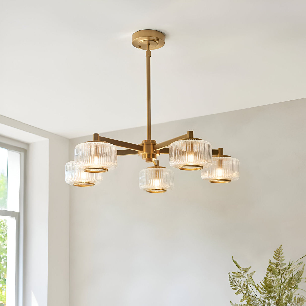 Rutland 5 Light Pendant in brushed aged brass with ribbed glass shades and telescopic stem, shown hanging in a living room setting.