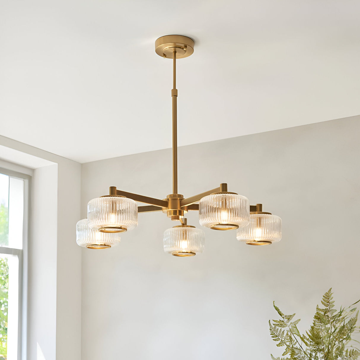 Rutland 5 Light Pendant in brushed aged brass with ribbed glass shades on a five-arm frame, shown hanging in a bright dining room setting.