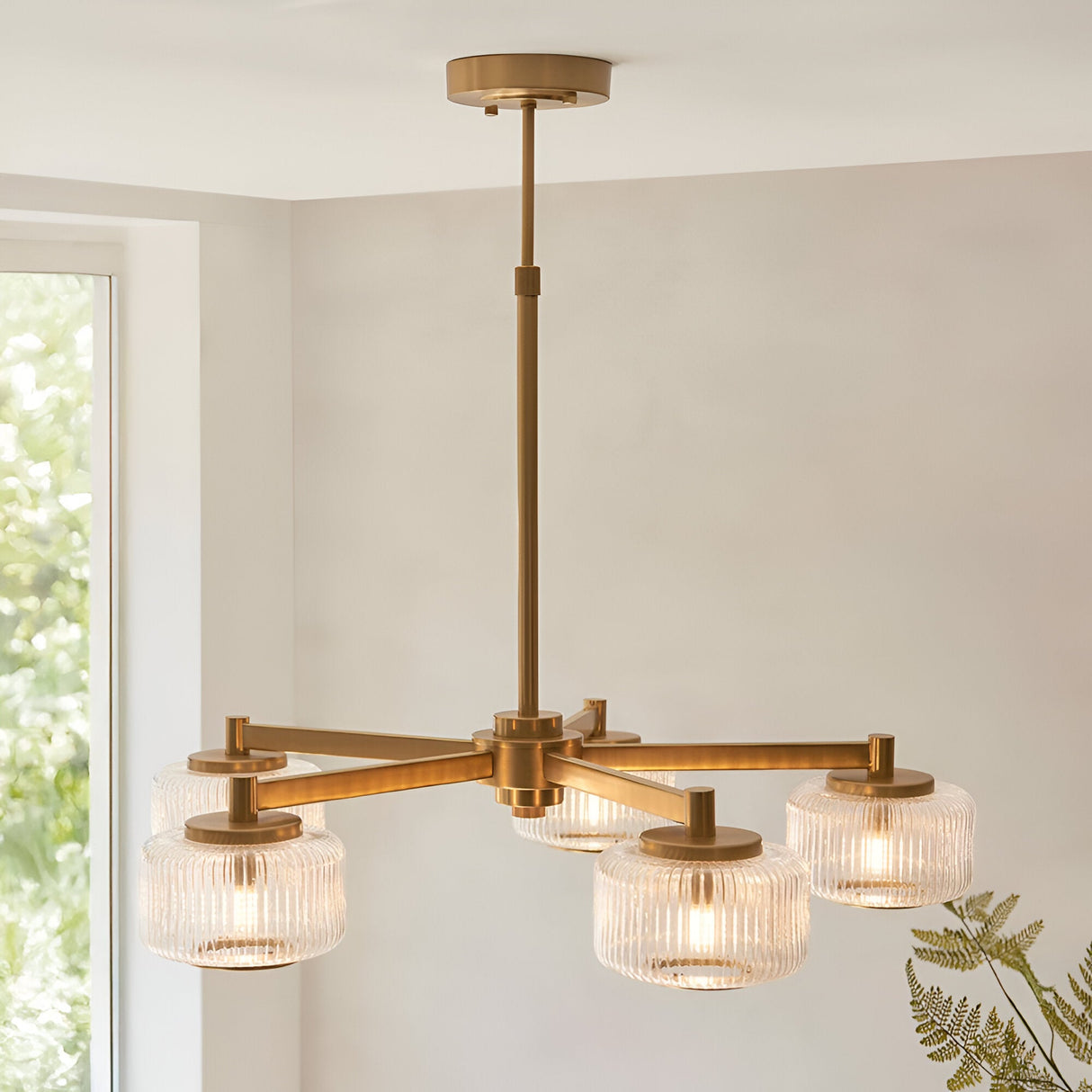 Rutland 5-Light Pendant in brushed aged brass, with ribbed glass shades on a central rod, shown suspended in a room with a window.