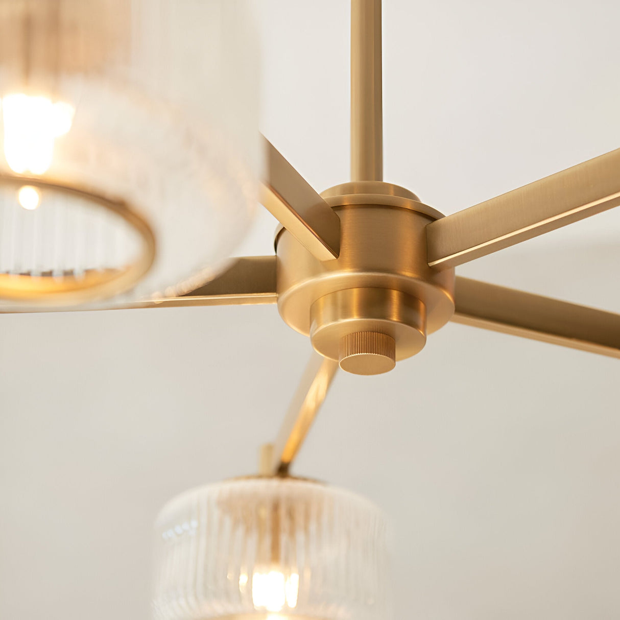 Close-up of the Rutland 5 Light Pendant in brushed aged brass, showing the central hub, splayed arms, and ribbed glass shades with metal trim.