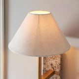 Bramble wall light with a tapered white fabric shade, brass-toned arm and natural stone backplate, mounted on a light wall.