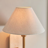 Bramble wall light with tapered linen shade, brass-toned arm and natural stone backplate, mounted against a plain light grey wall.
