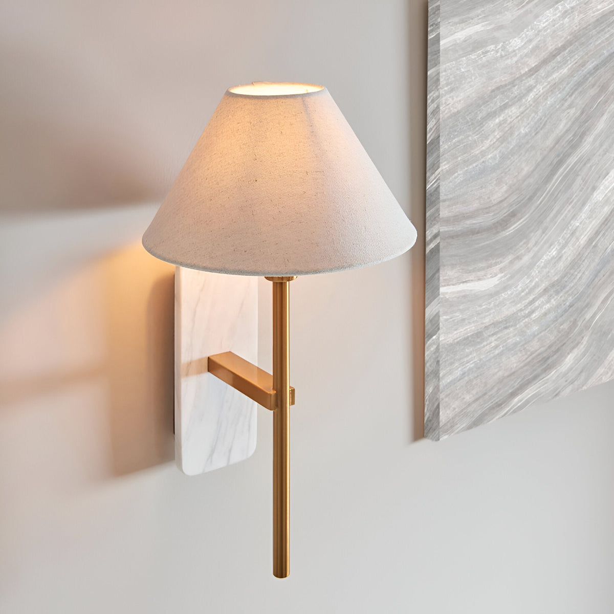 Bramble wall light with marble backplate, brass-toned arm and tapered natural linen shade, mounted beside a grey marble panel on a plain wall.