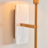 Bramble wall light with white marble backplate and brushed brass arm, mounted on a plain wall beside a matching brass floor lamp pole.