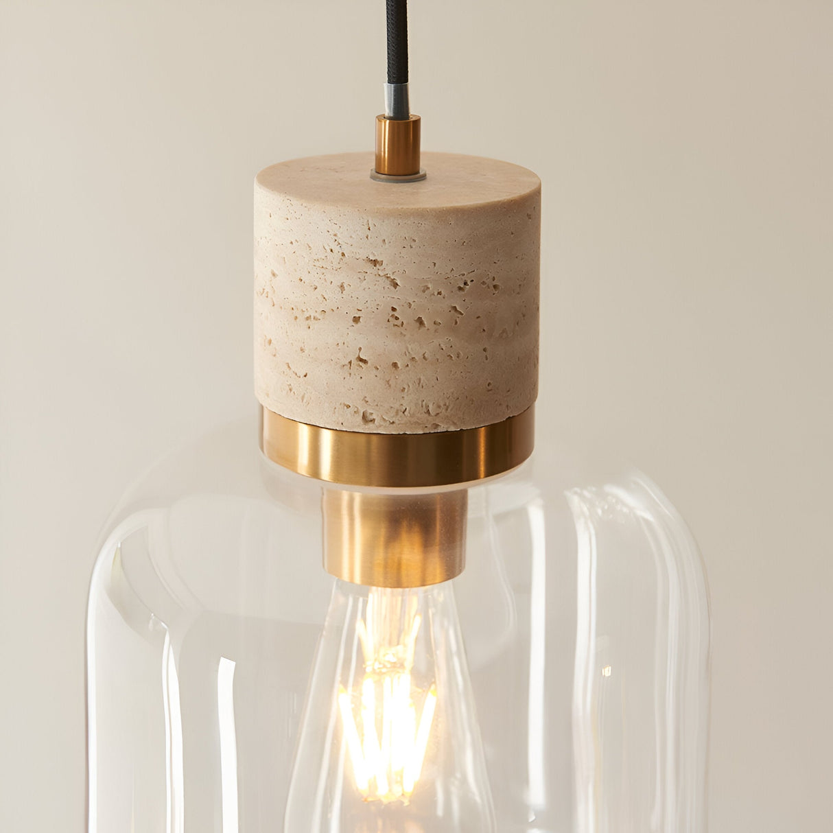 Endon Cranstead pendant light with beige travertine stone top, brushed brass collar and clear glass shade around a warm filament bulb.