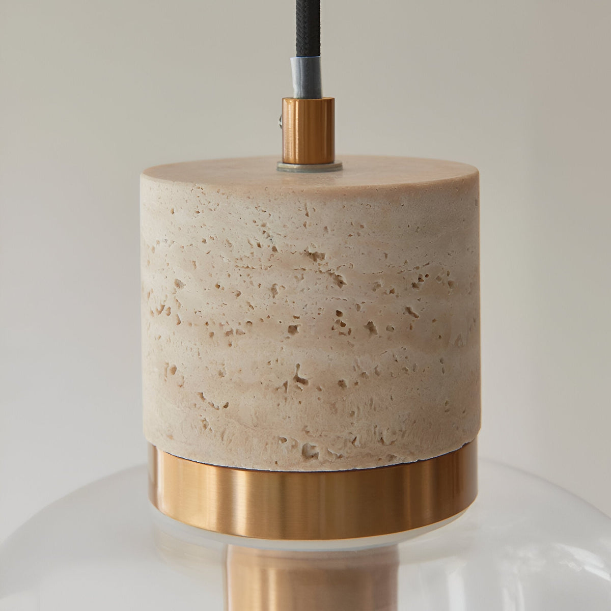 Close-up of Endon Cranstead Pendant Light showing beige travertine stone top, brushed brass collar and clear glass shade against a light background.