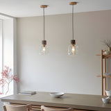 Cranstead pendant lights in brass and brown, with clear glass shades and marble tops, hanging above a dining table in a neutral-toned room.