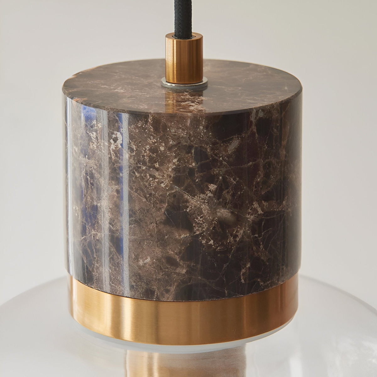 Cranstead Pendant Light with brown marble cylinder top, brushed brass collar, and clear glass shade on black fabric flex, shown on a white background.