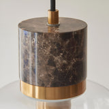 Cranstead Pendant Light with brown marble cylinder top, brushed brass collar, and clear glass shade on black fabric flex, shown on a white background.
