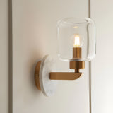 Cranstead Wall Light in brass with round white marble backplate, upright arm and clear glass shade revealing an exposed filament bulb.