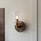 Cranstead wall light with dark brown Emperador marble backplate, brass arm and clear glass shade, mounted on a light wall.