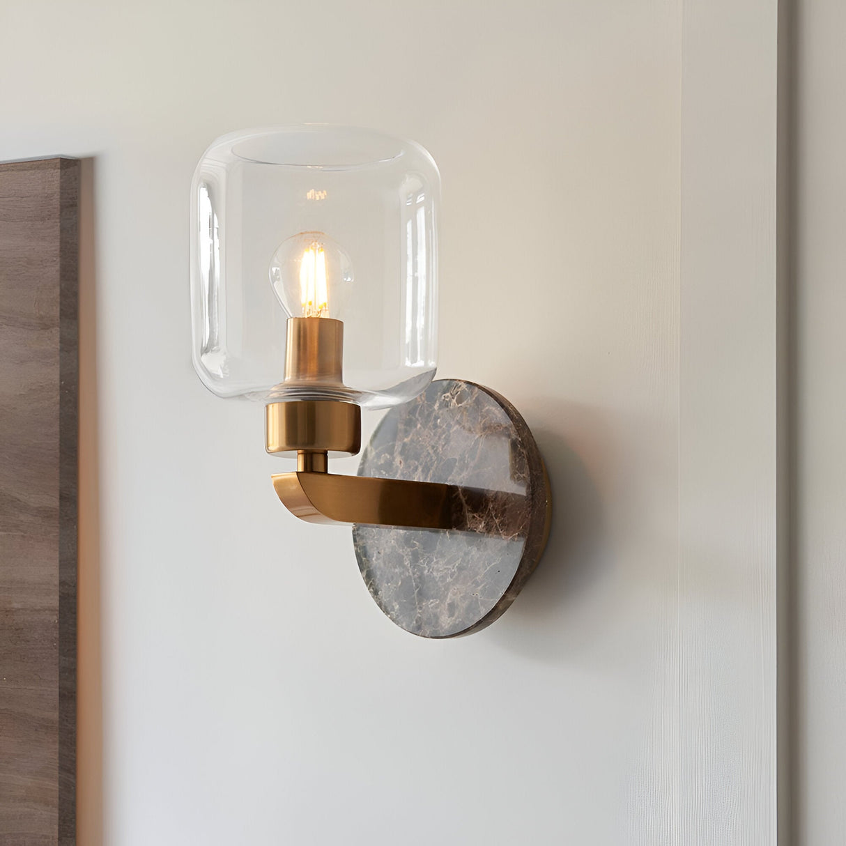 Cranstead Wall Light in Brass & Brown, single-light fixture with clear glass shade, brass arm and Emperador marble backplate, mounted on a light wall.