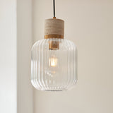 Cranton Pendant Light in brass and natural stone, with ribbed clear glass shade and black cord, hanging against a light wall.
