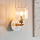 Cranton Wall Light in brass and white, with a round marble backplate, brass arm, and ribbed glass shade lit by an exposed bulb, shown mounted on a wall.