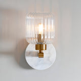 Cranton Wall Light in Brass & White with a round white marble backplate, brass arm and ribbed clear glass shade, lit against a plain light background.