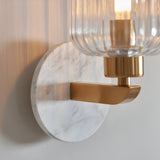 Cranton Wall Light in brass and white, close-up of the round marble backplate, brass arm, and ribbed glass shade against a plain wall.