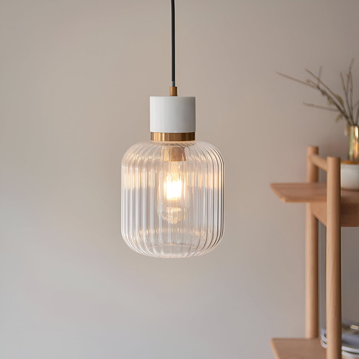 Cranton Pendant Light in brass and white, single E27 fitting with ribbed glass shade on black cord, shown lit beside a wooden shelf.