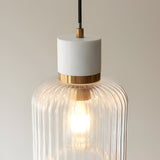 Cranton Pendant Light in Brass & White, close-up of white stone top, brass collar, and ribbed glass shade with visible E27 bulb, on a plain background.
