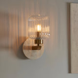 Cranton Wall Light in brass with a ribbed clear glass shade and natural travertine backplate, mounted on a light grey wall.