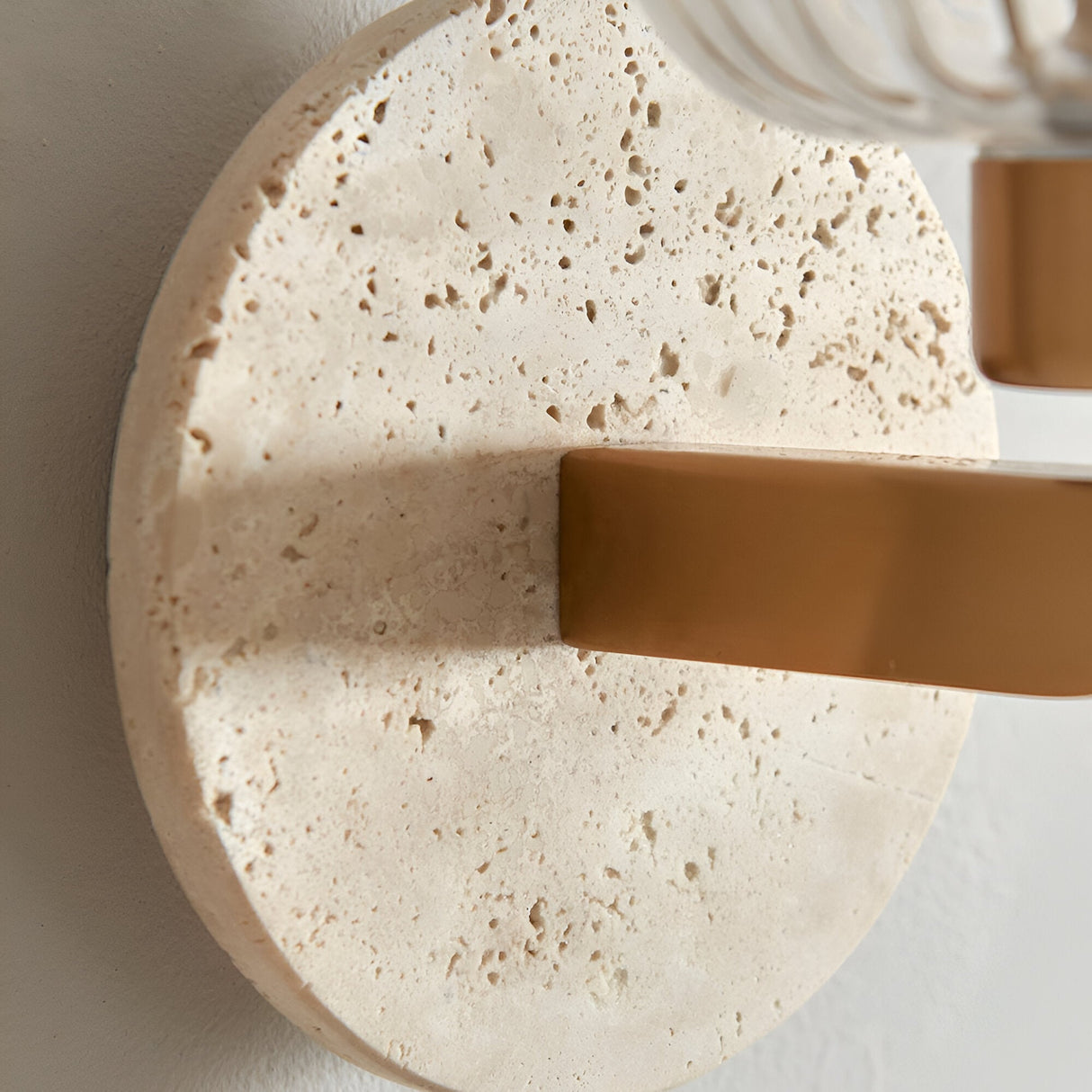 Cranton Wall Light with textured natural travertine backplate and brass arm, close-up detail against a white wall.