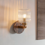Cranton Wall Light with brown Emperador marble backplate, brass arm, and ribbed clear glass shade, shown lit on a wall.