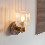 Cranton Wall Light in brass and brown, featuring a ribbed glass shade, brass arm, and Emperador marble backplate, mounted on a light wall.