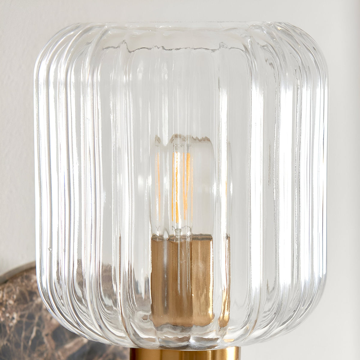 Cranton Wall Light close-up showing the ribbed clear glass shade, brass fitting, and exposed bulb, with a dark marble backplate visible below.