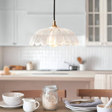 Endon Brackmont Carnation pendant light with a clear scalloped glass shade and brass fitting on a black cable, hanging above a bright white kitchen island.