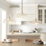 Endon Brackmont Carnation pendant lights with clear scalloped glass shades and brass fittings on braided cables, hung over a dining table in a white kitchen.