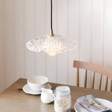 Brackmont Orchid Pendant with ribbed clear glass shade and brass fitting on black cable, hanging above a wooden dining table.