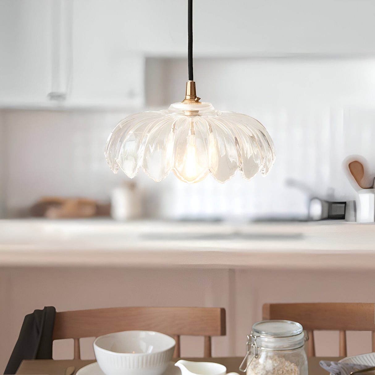 Brackmont Camellia pendant light with a scalloped clear glass shade and brass fitting on a black cable, shown lit above a kitchen dining table.