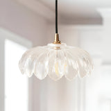 Brackmont Camellia Pendant with scalloped clear glass shade and brushed brass fitting on black cable, hung indoors above a light interior.