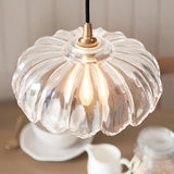 Brackmont Camellia pendant light with scalloped clear glass shade and brushed brass fitting on black cable, shown lit above a kitchen table.