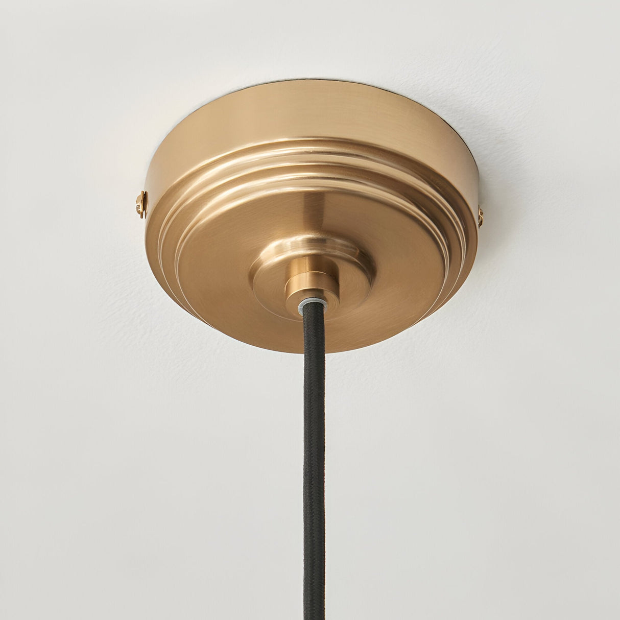 Brackmont Camellia Pendant ceiling canopy in brushed brass with black braided fabric cable, shown close-up against a plain white ceiling.