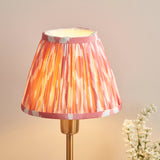 Endon Cliffbourne Ikat table lamp with a pleated coral pink and white ikat-print faux silk tapered shade on a stepped brushed brass base.