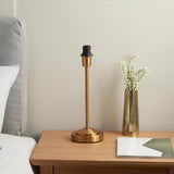 Endon Cliffbourne table lamp base in brushed brass with stepped base and E14 fitting, shown shadeless on a wooden bedside table beside a brass vase.