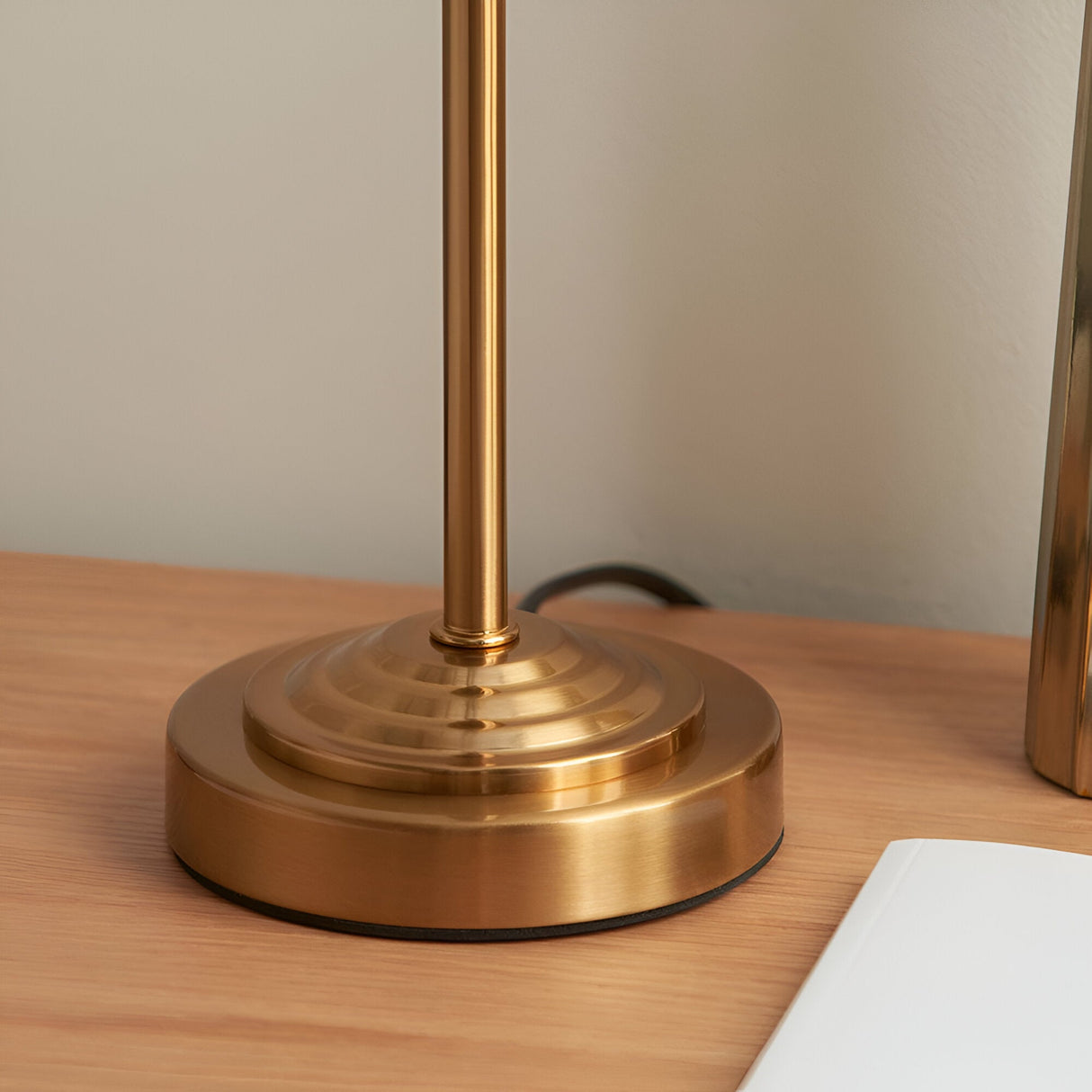 Close-up of the brushed brass stepped base and slim stem of the Endon Cliffbourne Ikat table lamp on a light wood surface.