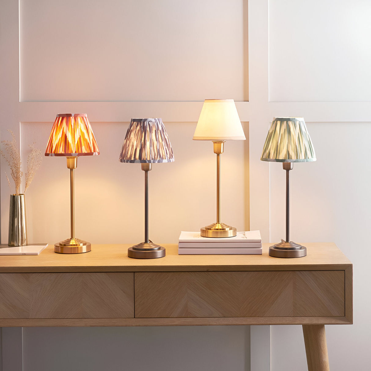 Endon Cliffbourne table lamps on an oak console with pleated Ikat shades in coral pink, grey, green and white on brass and bronze bases.